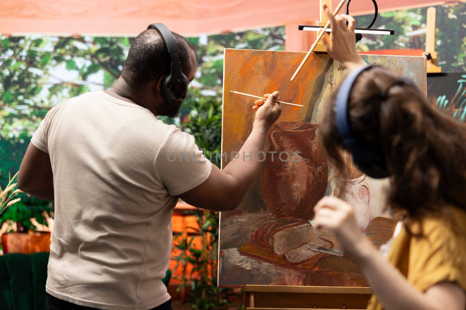 Team of artists painting a beautiful rustic creation on canvas, mixing colors together on a palette to create a nature inspired design. Diverse painters enjoy quality time in art studio.