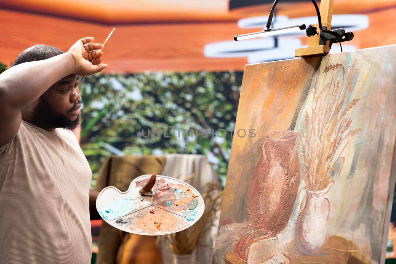 African american painter feeling tired after painting a new colorful artwork, working hard to create a modern beautiful masterpiece for the gallery exhibition. Young artist in his creative process.