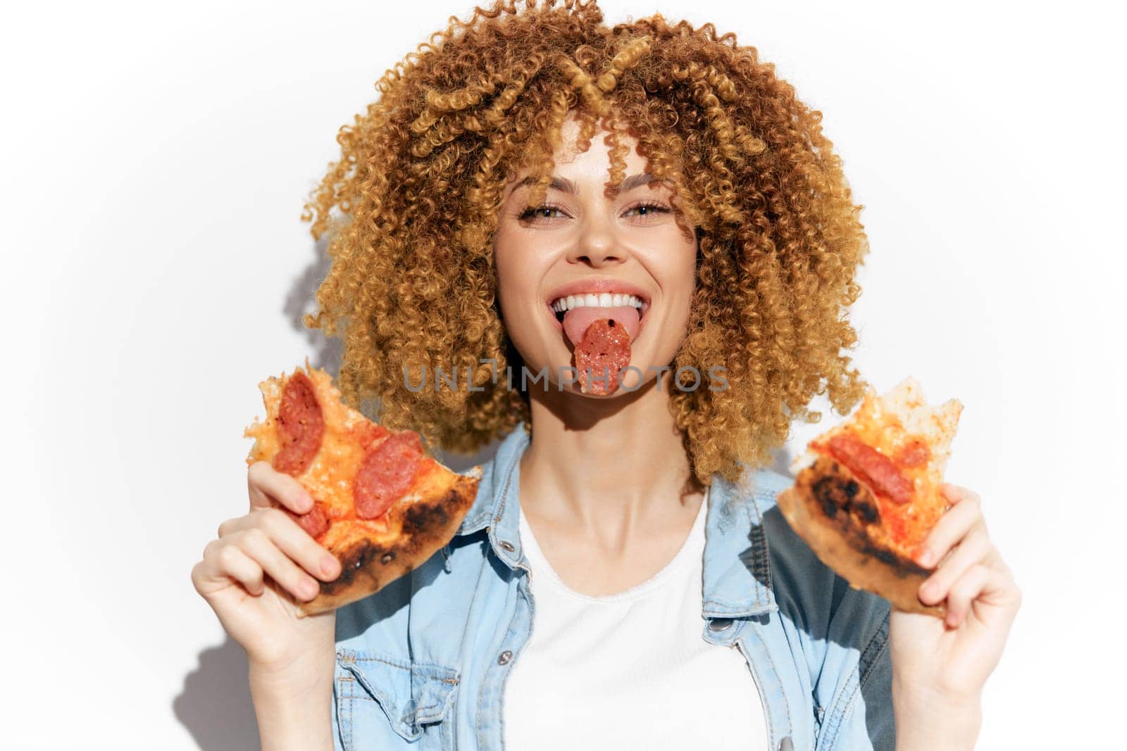 Energetic woman with curly hair playfully eating pepperoni pizza, embodying joy and indulgence, perfect for food related themes and seasonal festivities