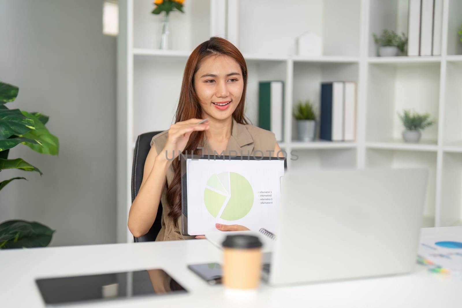 Focused on her analysis, a business professional reviews data while seamlessly conducting a remote meeting, demonstrating multitasking in a modern workspace.