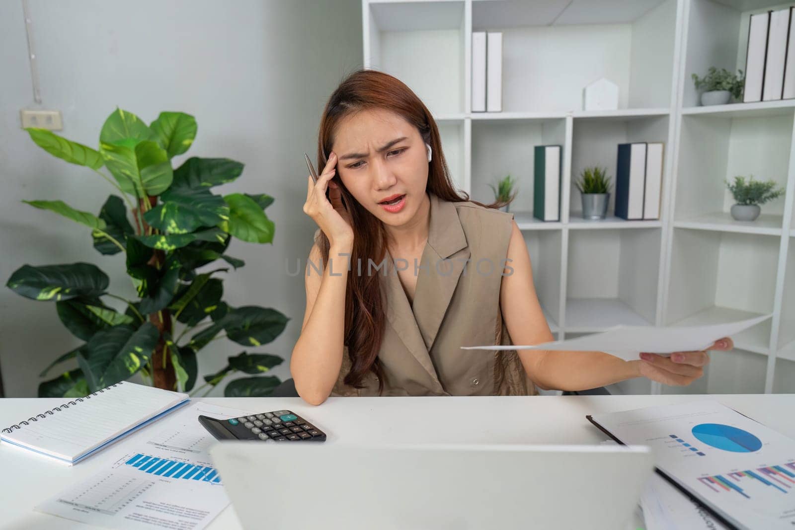 Amidst her workspace, a woman shows visible signs of strain while managing difficult financial information, emphasizing the challenges faced in the modern work environment.