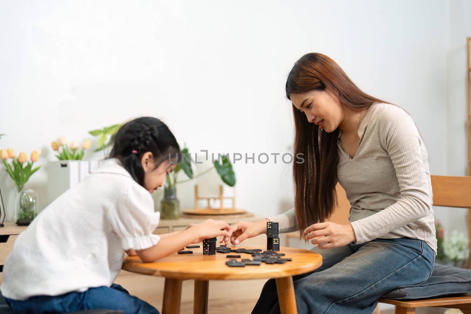 In a cozy home setting, a mother and daughter engage in a fun board game, fostering skills and bonding. Their focus on the game highlights the enriching experience.