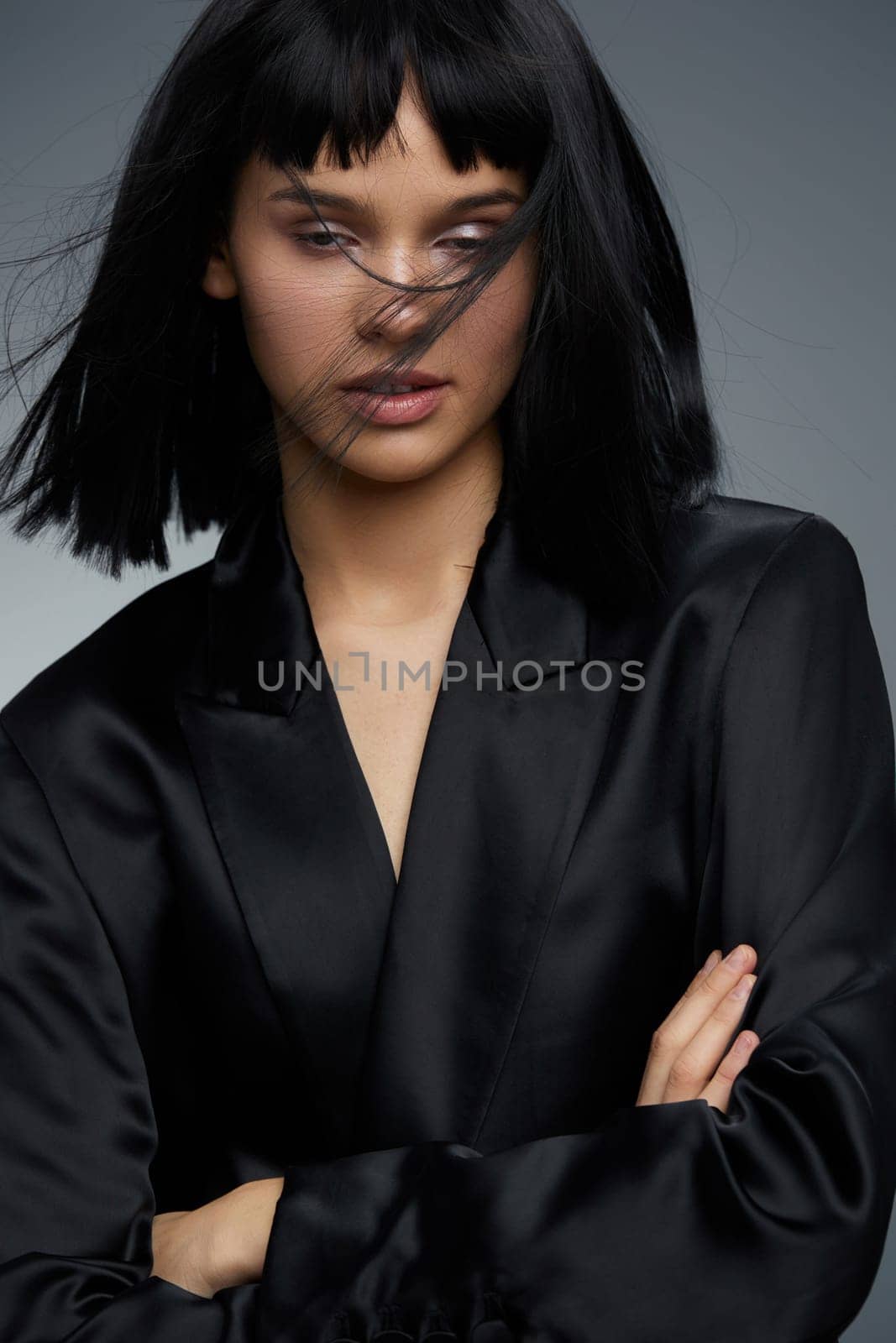 Blackhaired woman in black blazer posing confidently for the camera with arms crossed and hair flowing in the wind