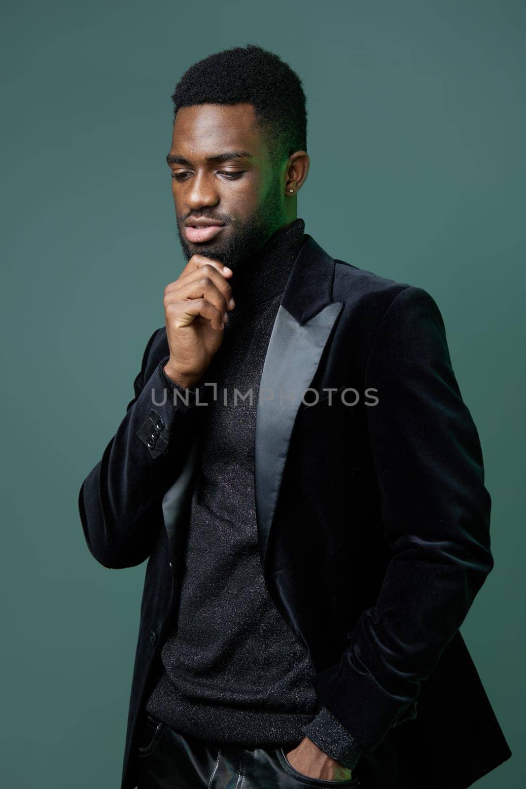 A confident young man in a black suit, hand on chin, gazing intently at the camera, deep in contemplation.