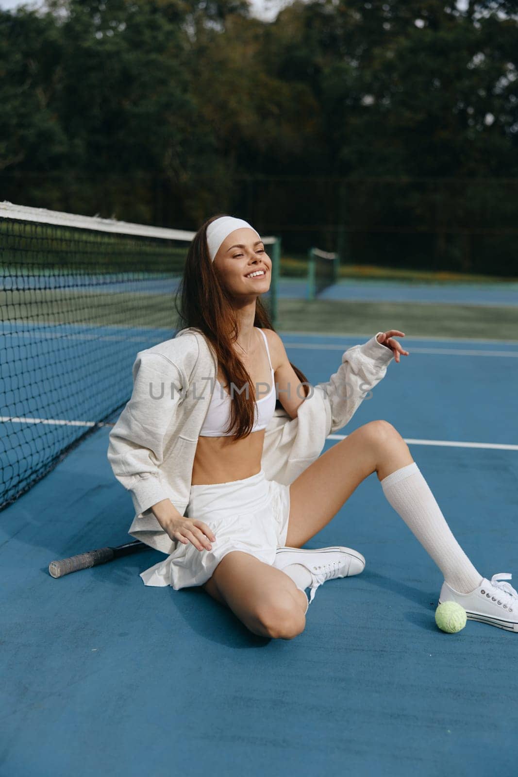 A young female tennis player enjoying a moment of joy on the court, wearing sporty attire, conveying energy and confidence against a blue backdrop, perfect for sports themed projects