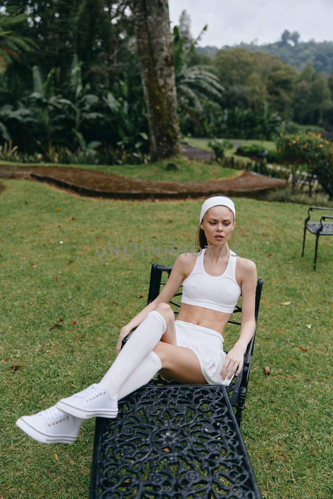 A young woman exudes tranquility while wearing modern white activewear, resting in a lush garden, symbolizing wellness, relaxation, and a healthy lifestyle