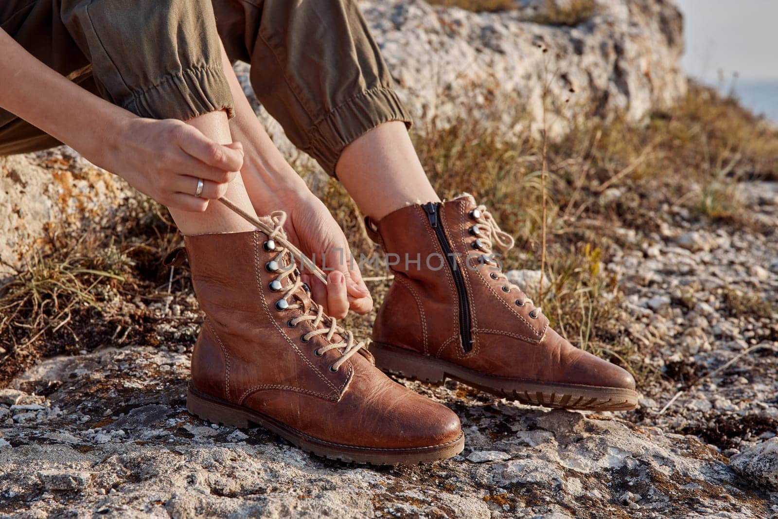 Woman tying boots on rocky hillside with ocean background travel adventure beauty nature scenery trip discovery wild exploration outdoor activity