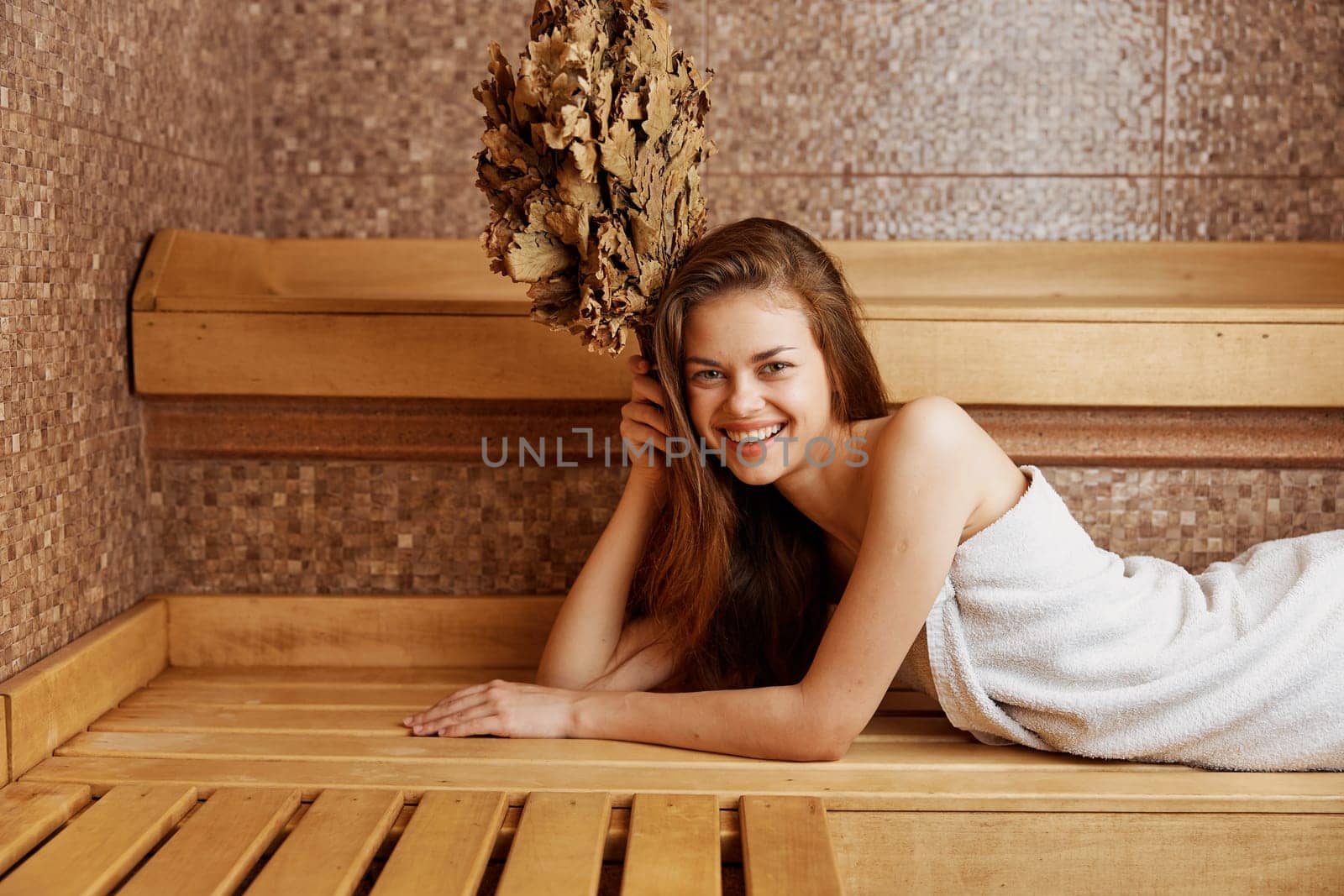 Relaxing in the sauna woman in towel lounging on bench with plant on head