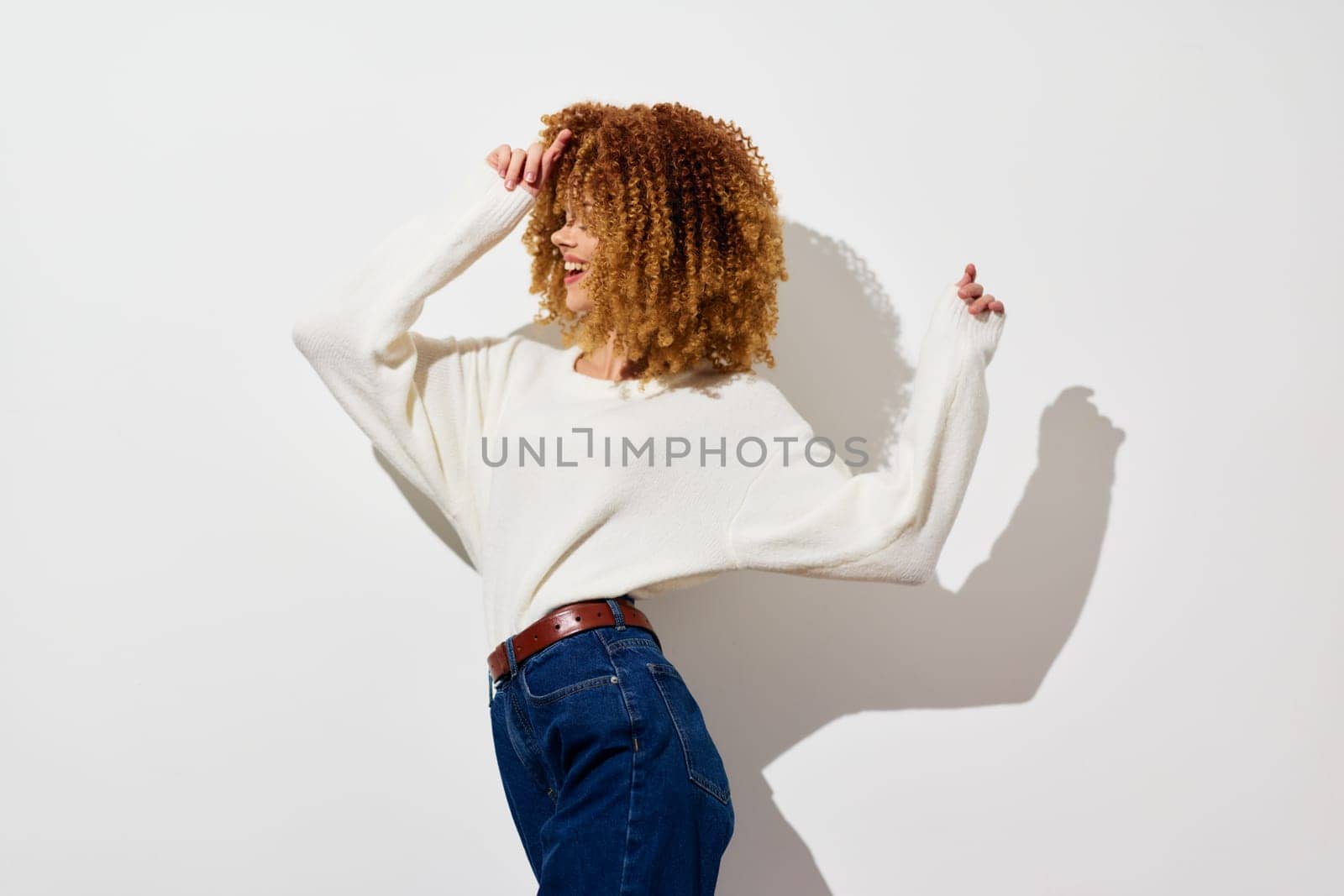 A joyful young woman with curly hair is playfully posing in casual attire against a bright white background She exudes confidence and a relaxed vibe, embodying modern fashion and lifestyle trends