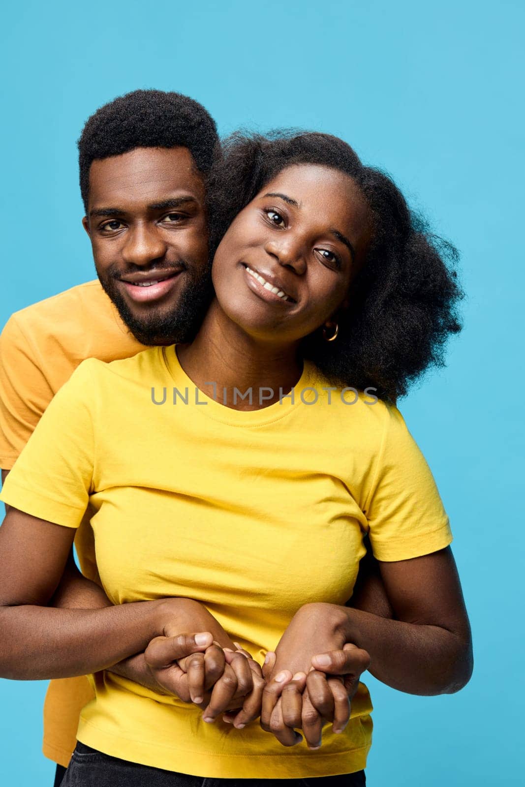 A joyful young African couple wearing matching yellow t shirts stands together against a bright blue background, symbolizing love and togetherness Their smiles convey happiness and connection