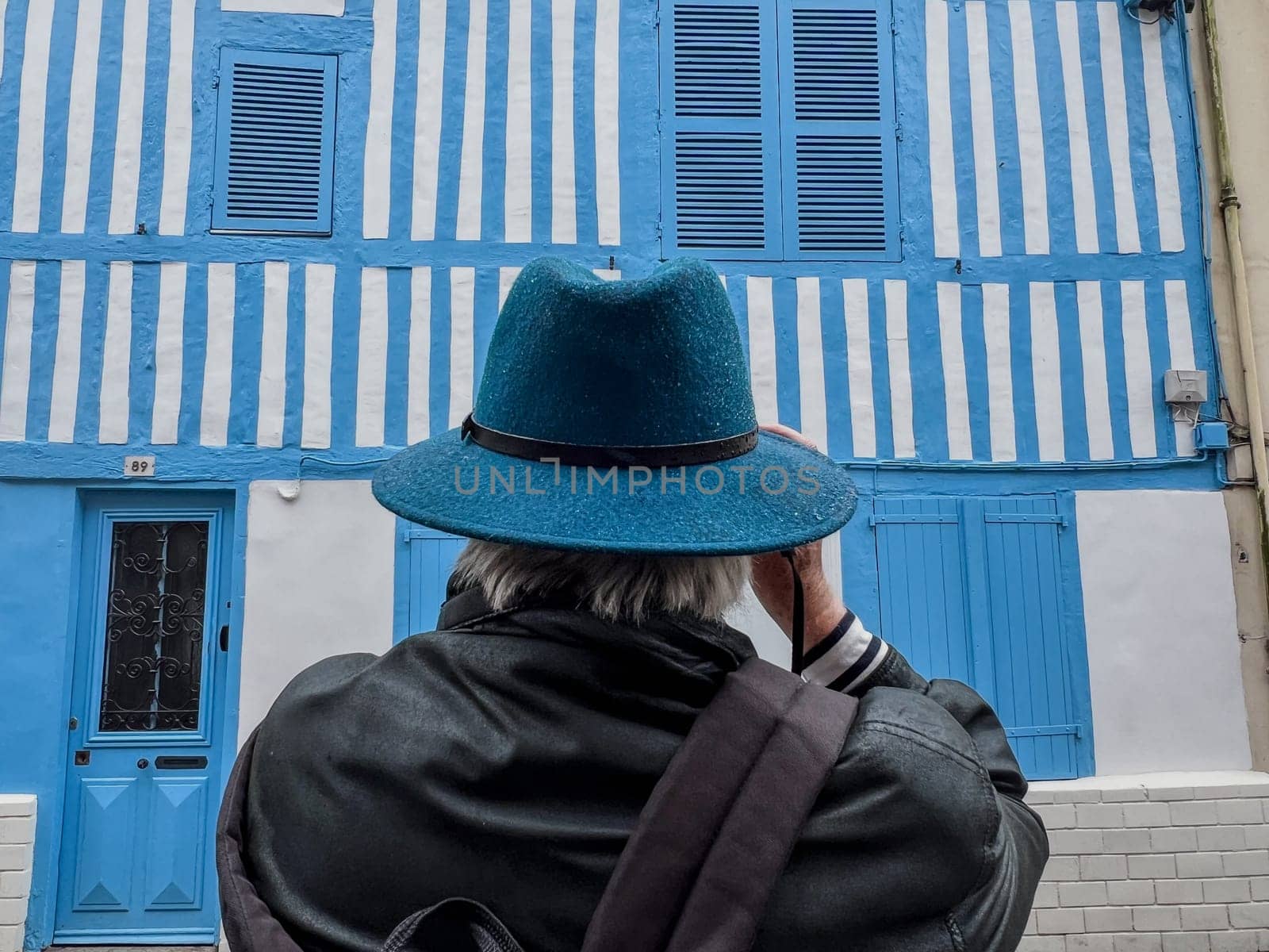 Back of a male tourist photographer with blue hat photographing historical blue landmarks in Honfleur, Architectural Blue House, High quality photo