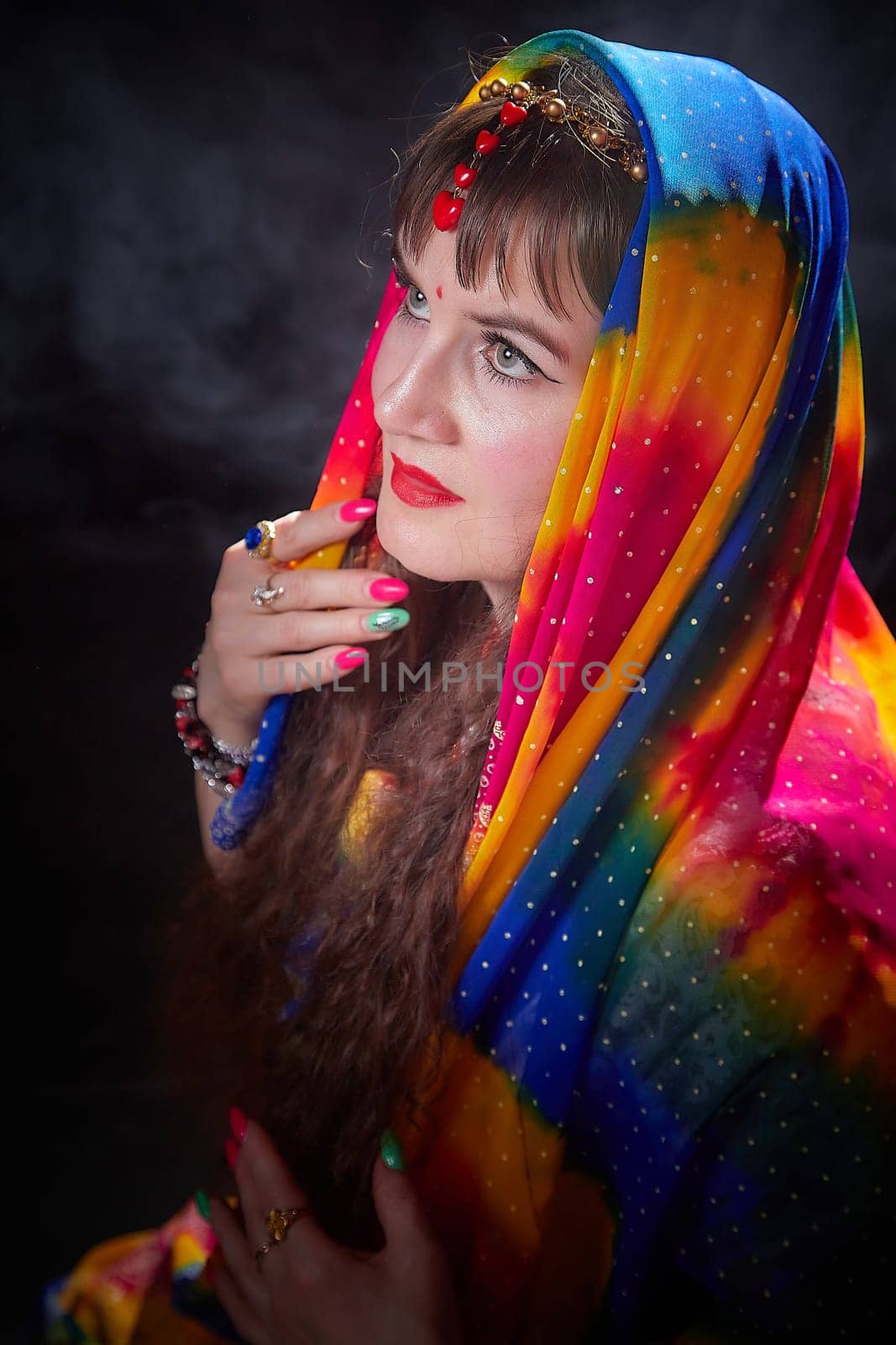 A mature woman showcases her beauty in a vibrant sari while posing in an artistic Indian themed setting.