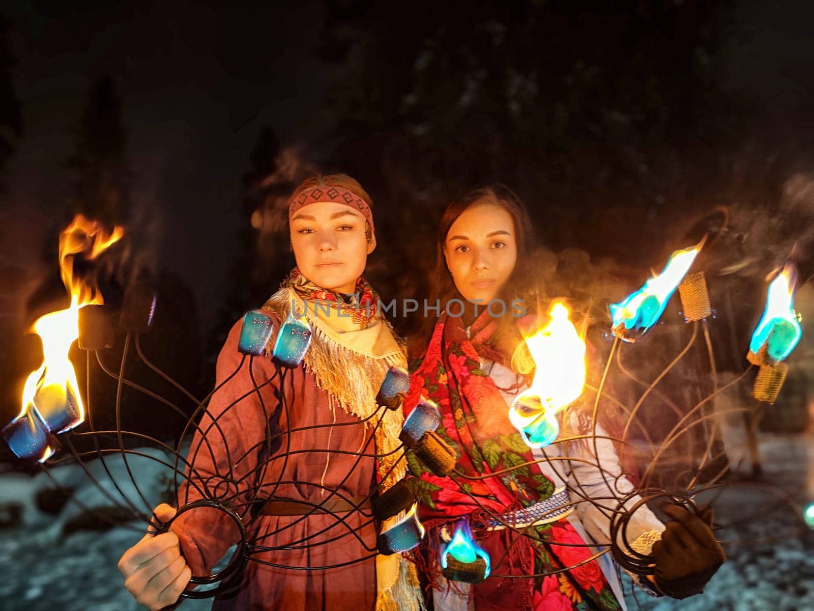 Vibrant actors perform an awe-inspiring fire show in ethnic costumes amidst a cold winter night, captivating the audience with their skill.