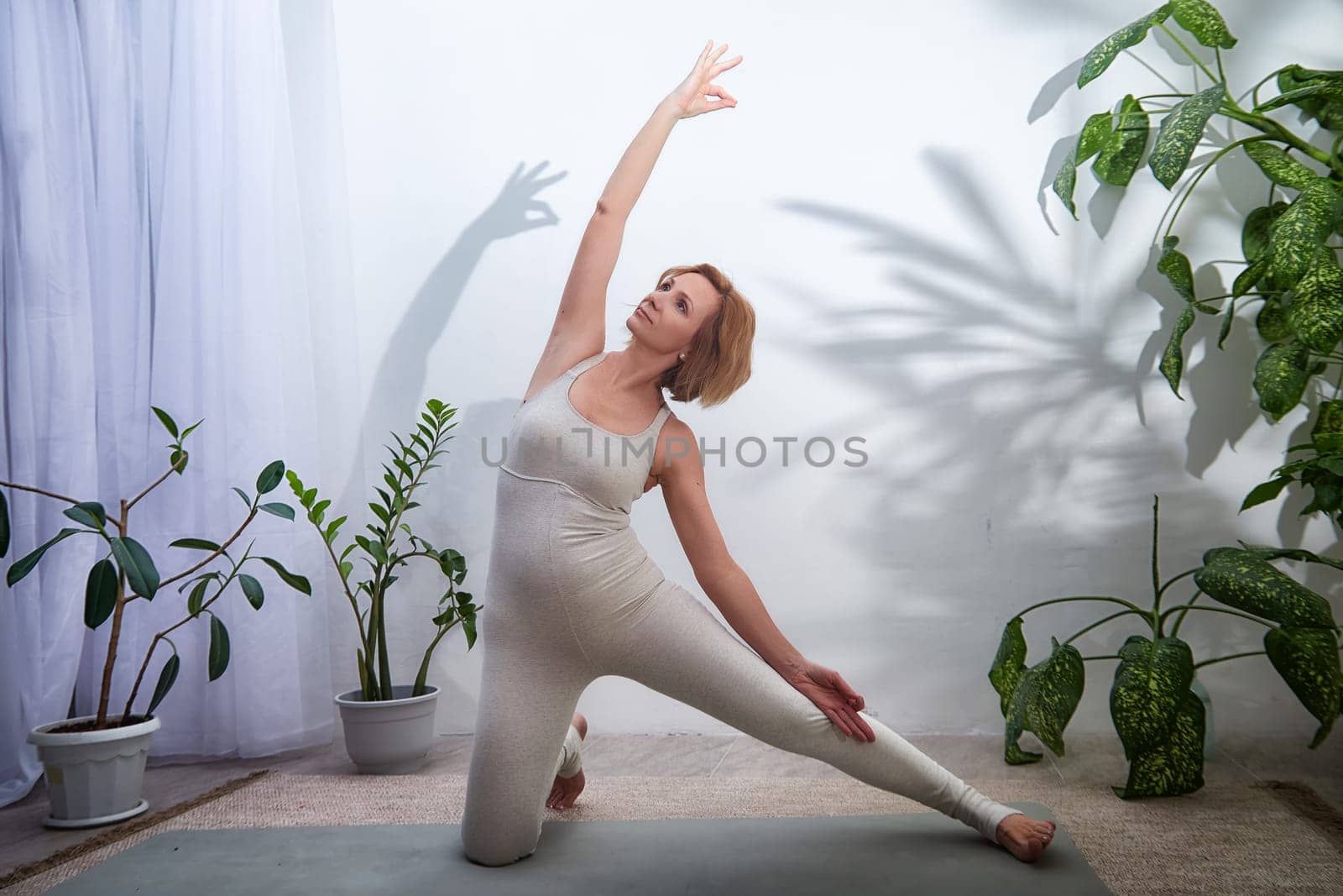 A woman performs a yoga pose in a calming indoor setting filled with plants, focusing on balance, strength, and relaxation.