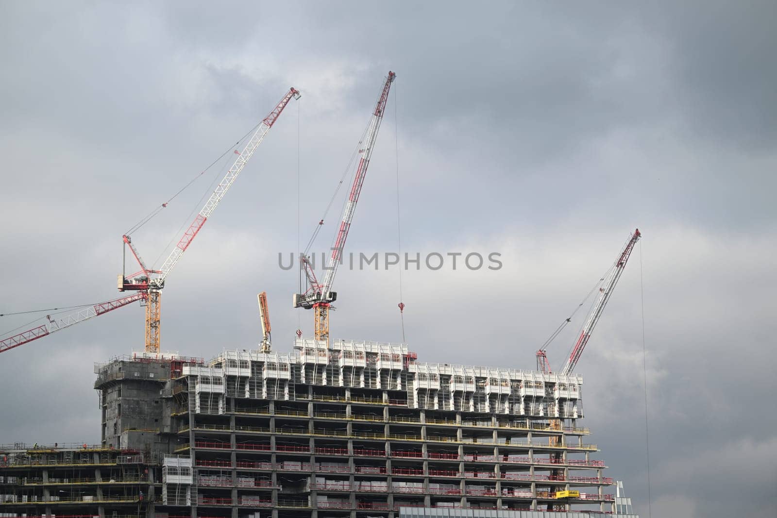 Cranes operate at a construction site in Paris, where workers are actively involved in the development of a modern high-rise building under overcast weather.