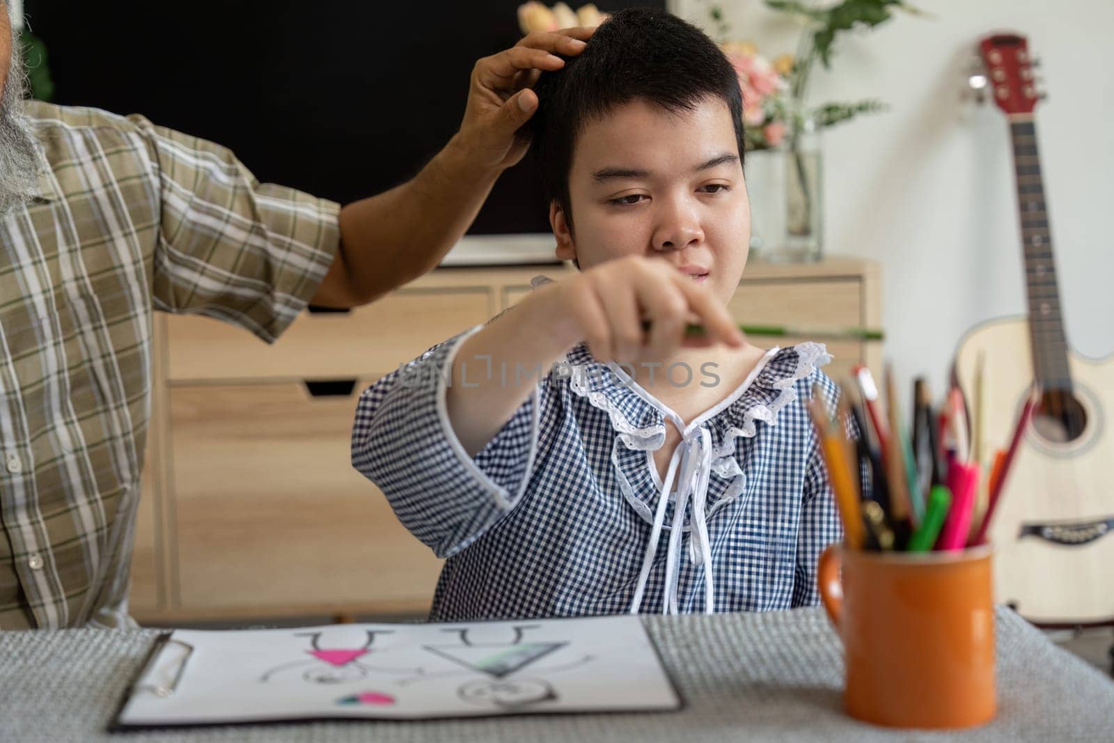 The teenage girl with Down syndrome collaborates with her grandfather on an art project, fostering creativity and family bonding.