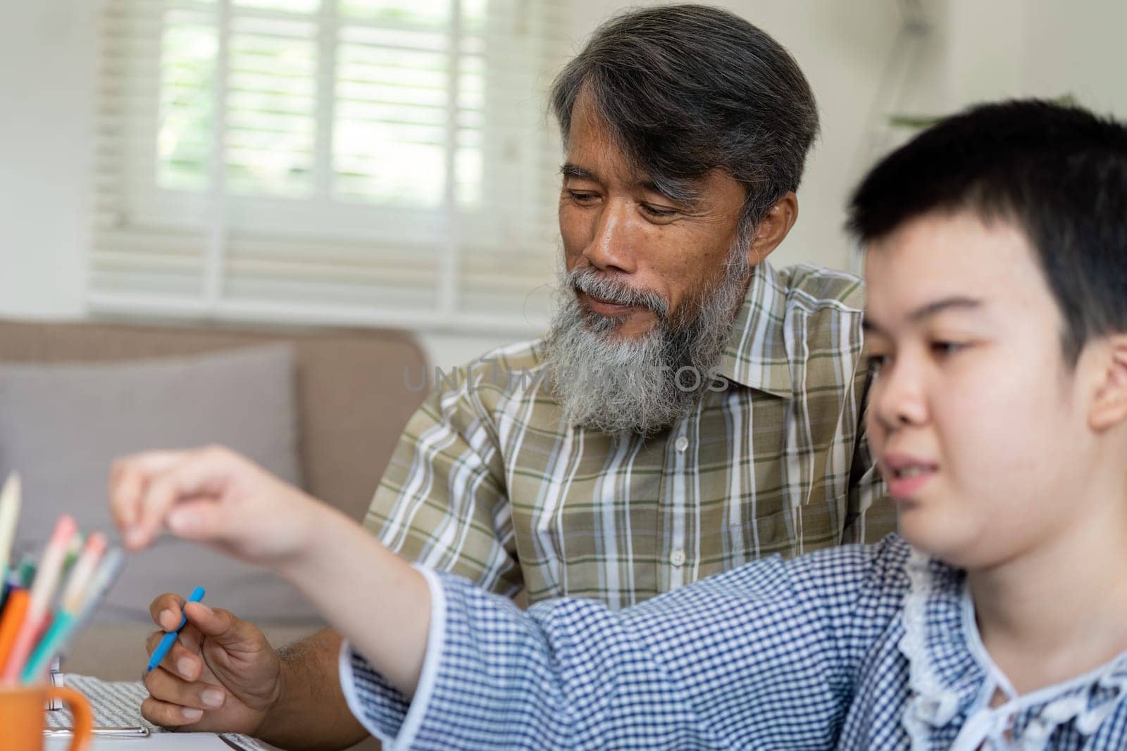 In a nurturing environment, a teenage girl with Down syndrome is deeply engaged in her drawing, with her grandfather providing guidance and encouragement during their art session.
