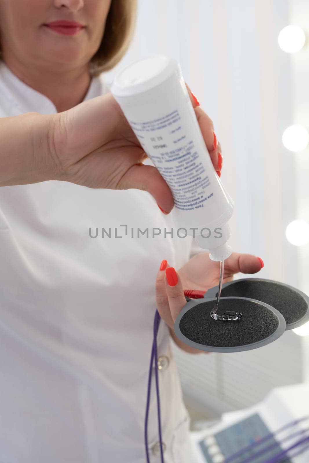 Crop unrecognizable masseuse in white medical robe electronic anti cellulite pads in modern clinic