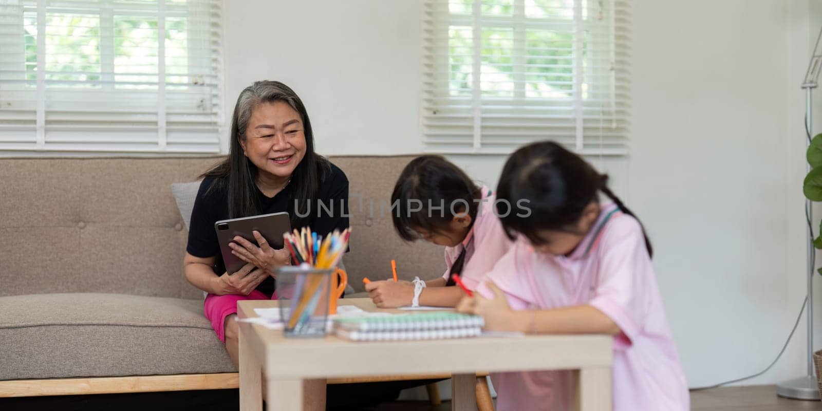 A caring grandmother helps her granddaughters with their schoolwork, fostering a nurturing learning environment. The scene emphasizes the importance of family support in education.