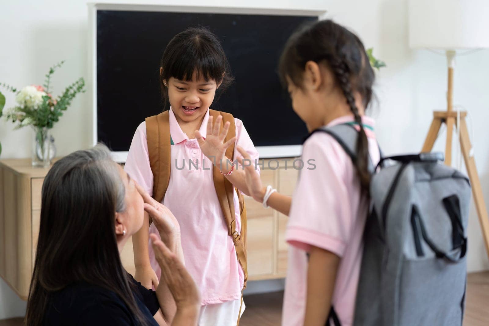 Two children joyfully wave goodbye to their caregiver, capturing the spirit of excitement and anticipation for a new school day.