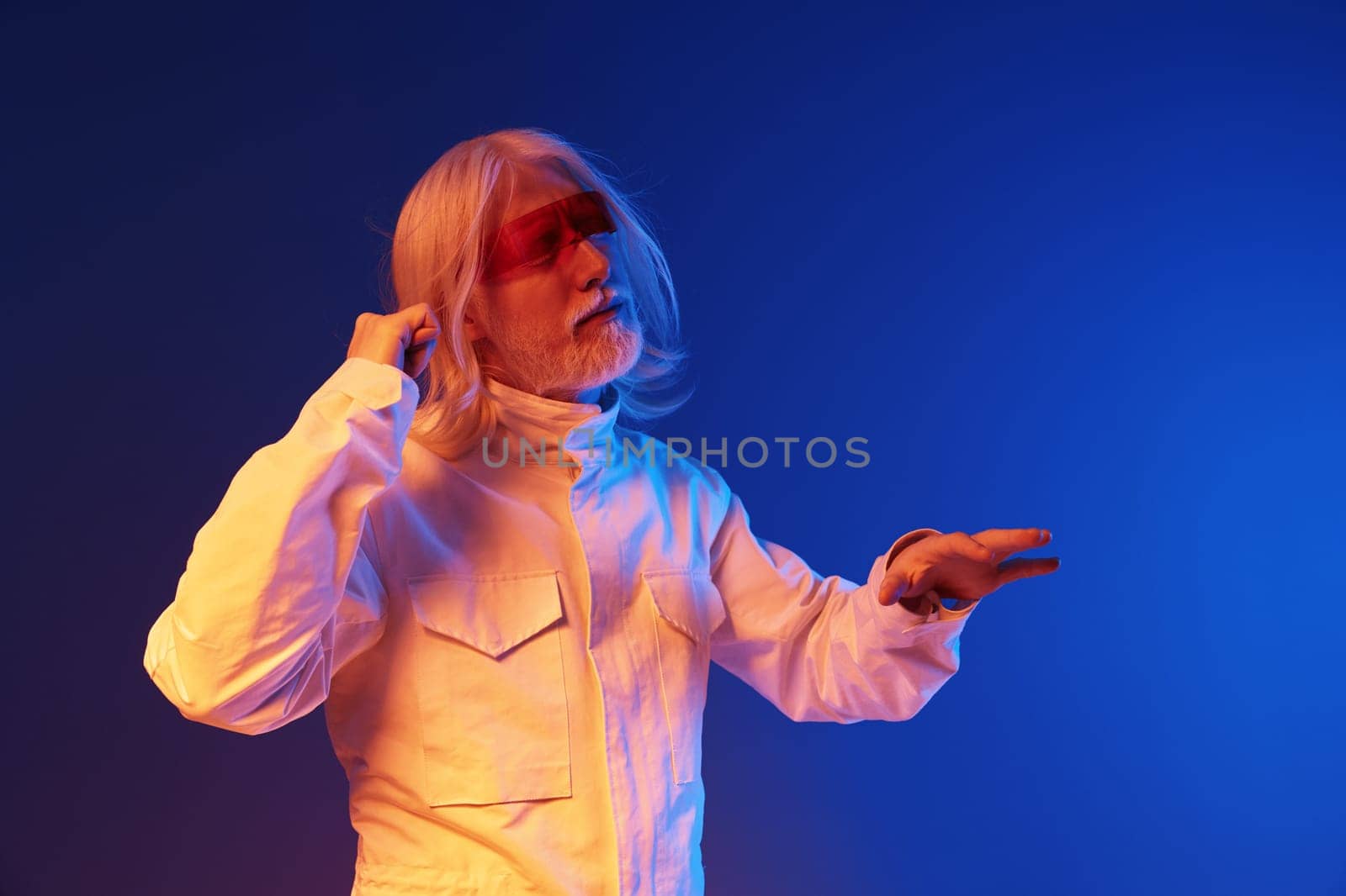 dynamic scene featuring an elderly man dressed in a contemporary outfit, engaging with colorful lighting The background blends blue and orange hues for an artistic, modern feel, emphasizing creativity
