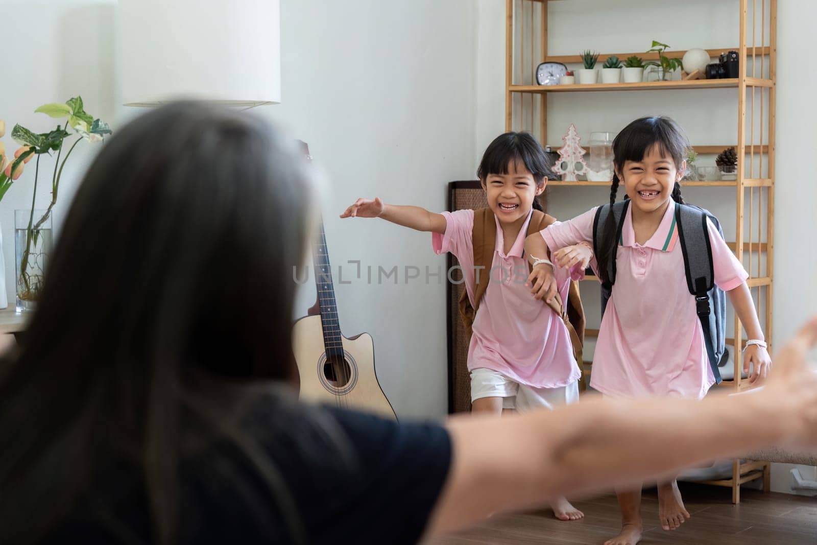 Two cheerful sisters, dressed in their school uniforms, rush into the living room to greet their grandmother, showcasing the joy of returning home after a day at school.