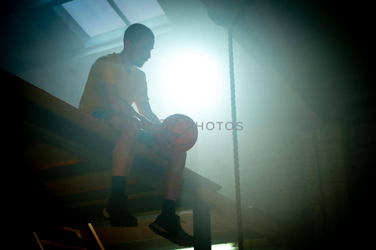 A silhouette of a young basketball player sitting with a ball, surrounded by dramatic lighting effects.