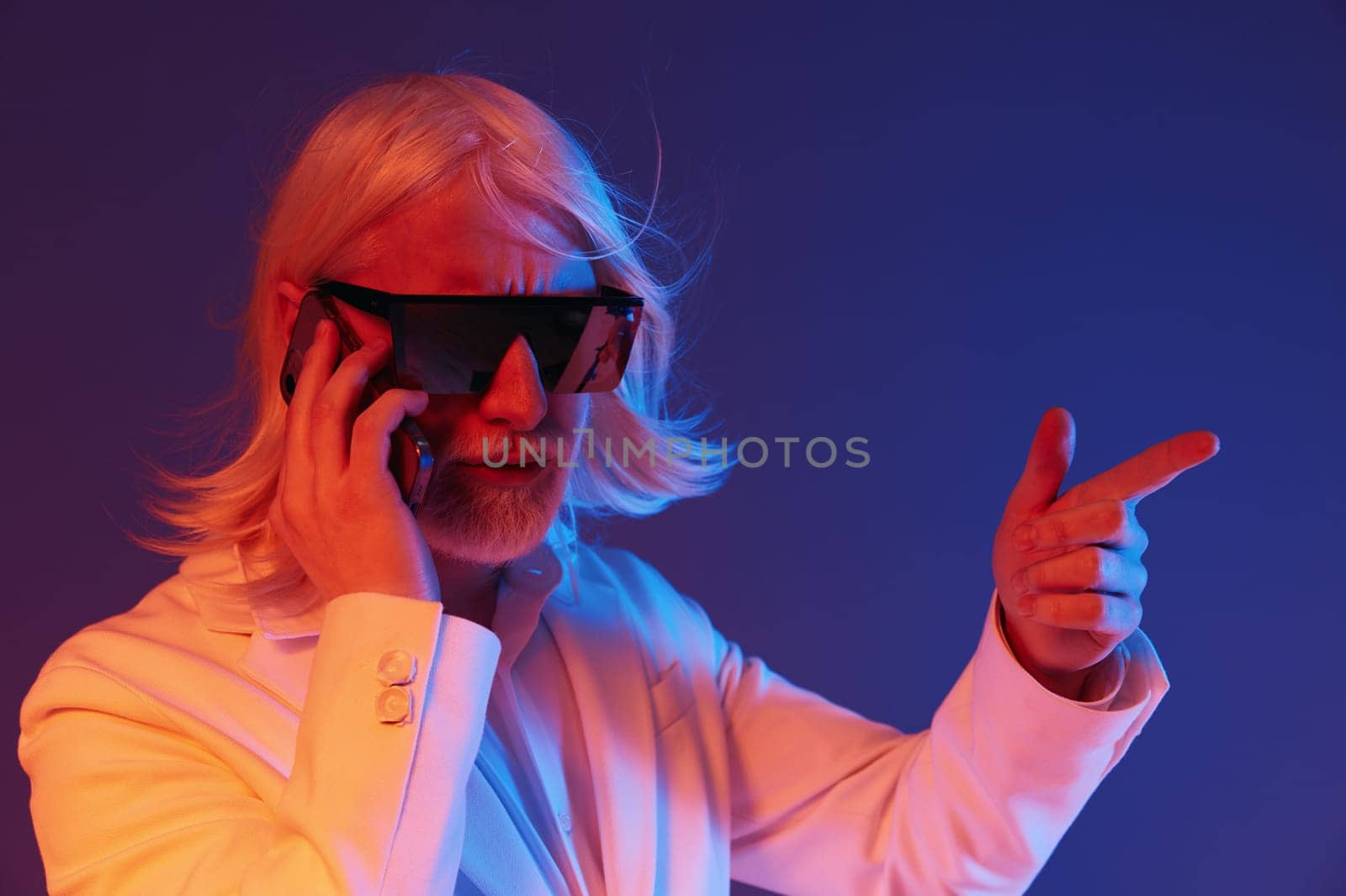 Confident businessman in sunglasses making a call and gesturing, set against a vibrant blue and purple background The image captures a sense of modernity and professionalism