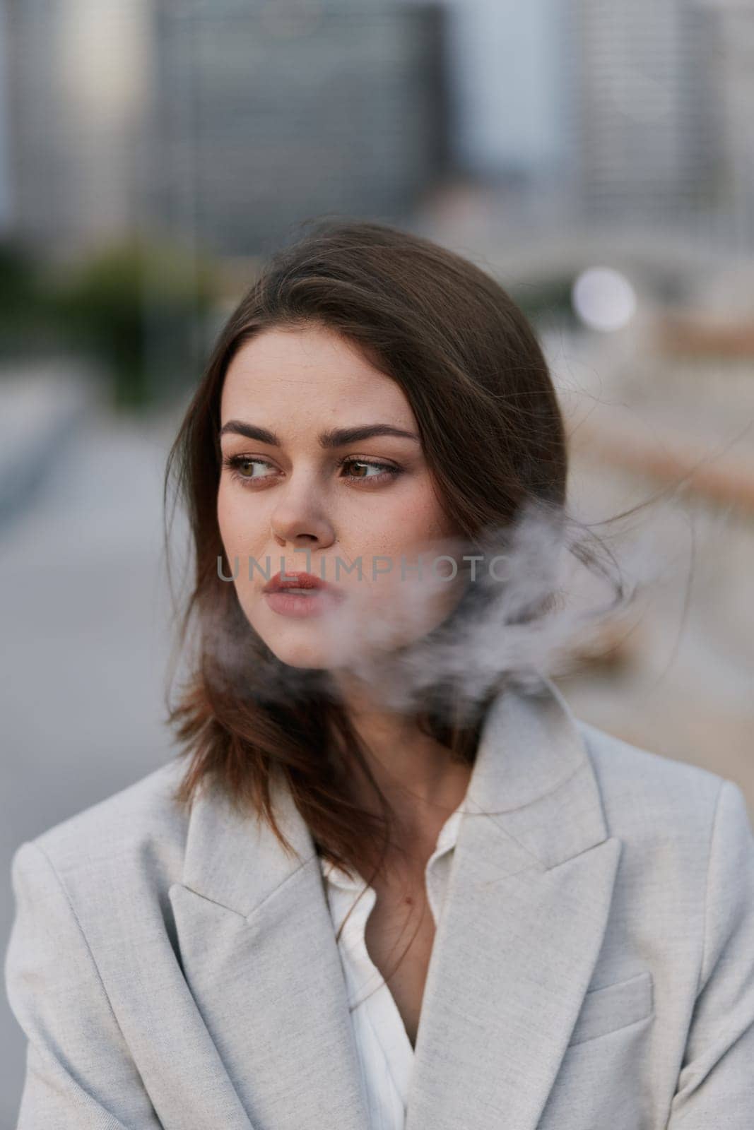 Thoughtful young woman in light gray blazer with smoky effect, standing outdoors in urban city background, conveying emotional business and psychological challenges.