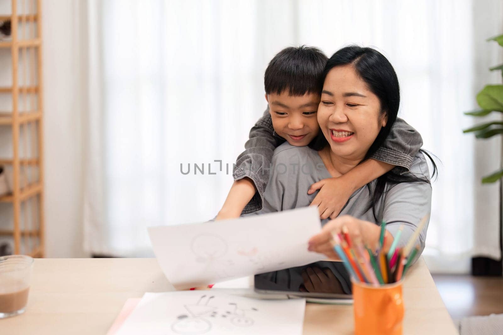 A mother and her son share a warm embrace while looking at his artwork, highlighting the joy of creativity and family connection during school preparations.