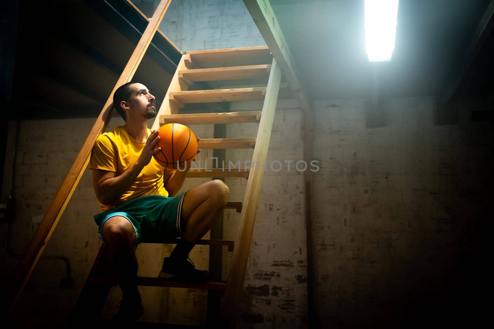A basketball player is lost in thought within a moody atmosphere, capturing a moment full of reflection and passion