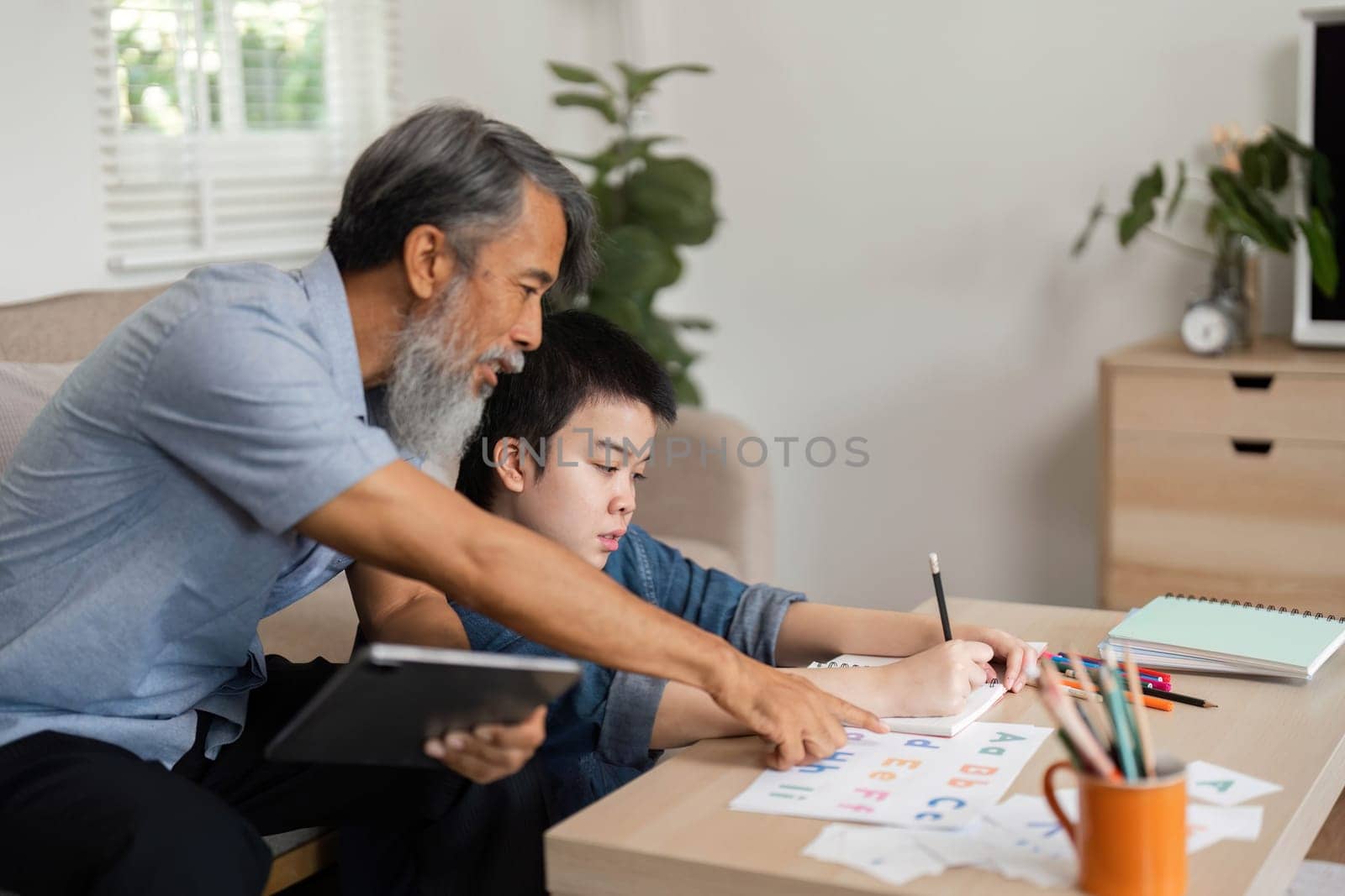 A grandfather shares quality time with his grandson, using interactive learning tools to teach letters and foster a love for learning in a warm home setting.