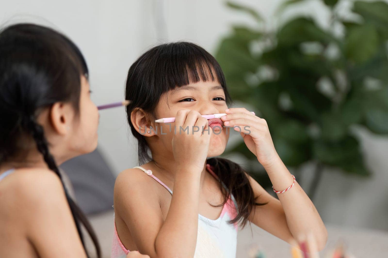 Two girls share a playful moment as one holds a pencil to her face, highlighting their creative spirit during an art session. Their laughter and expressions embody the joy of childhood.