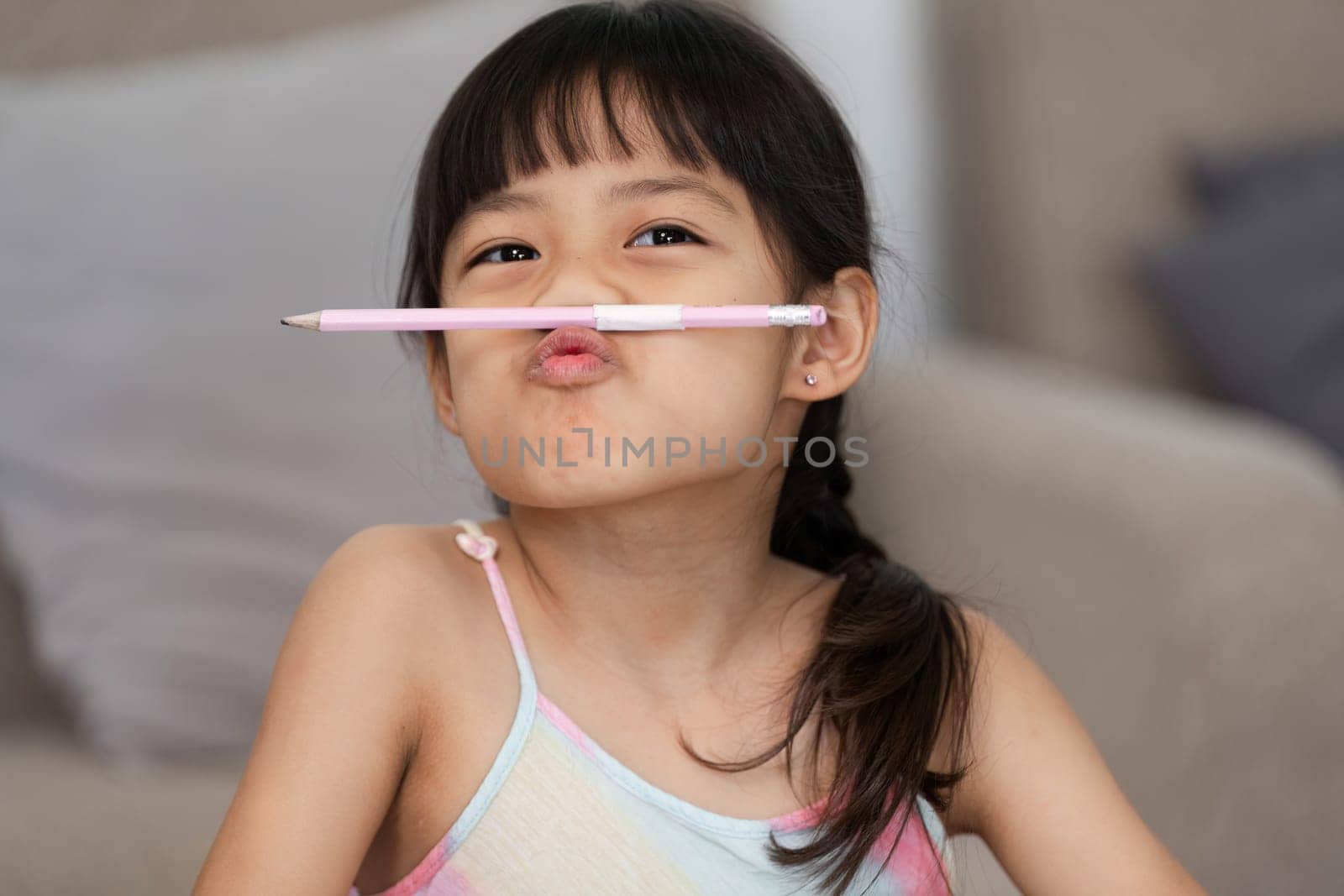 A young girl playfully balances a pencil on her nose, expressing her silly side while enjoying an art session with friends. This moment captures the joy of childhood and creativity.
