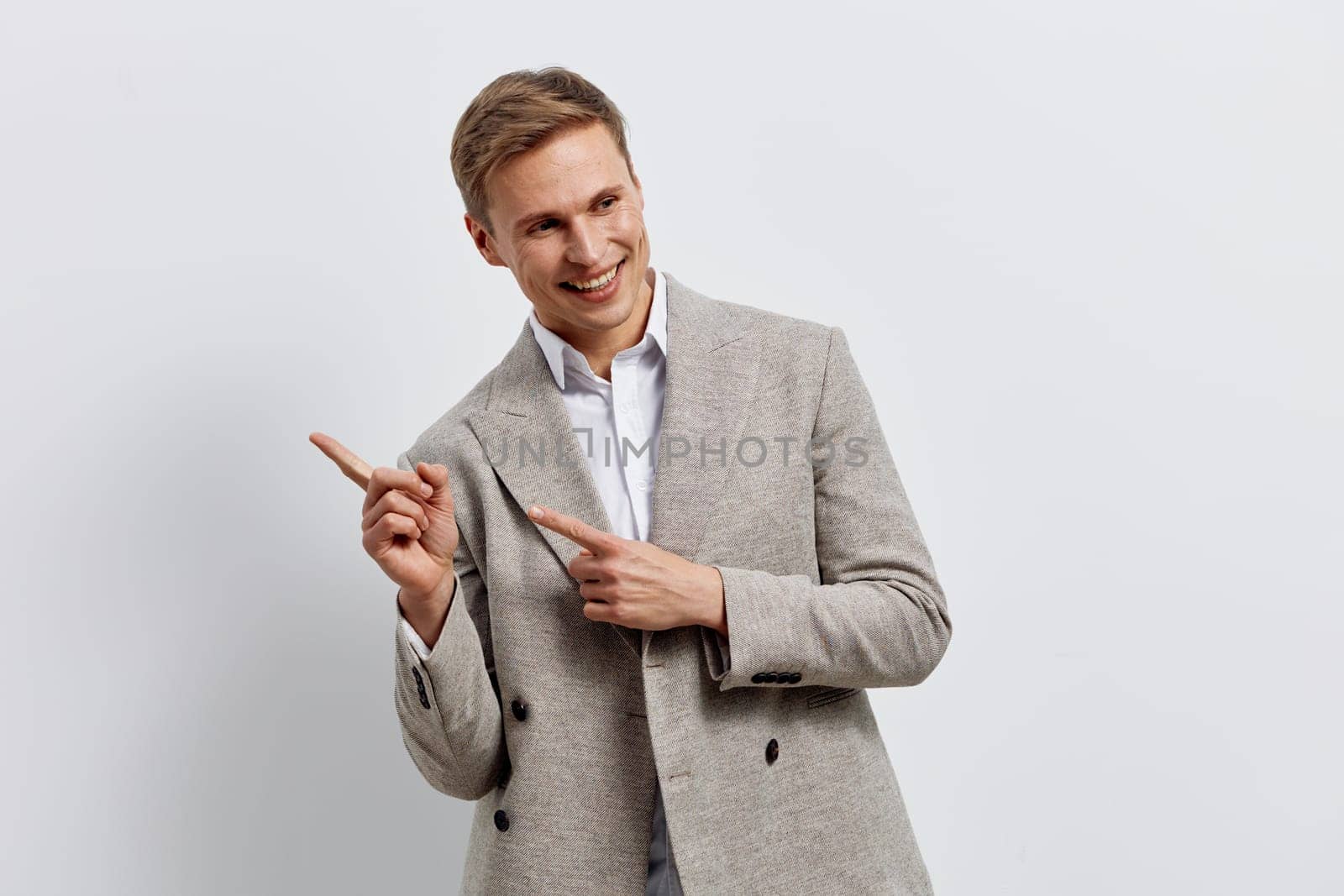 Smiling man wearing casual jacket pointing fingers sideways showing positive emotion and enthusiasm in a bright studio setting. He represents creativity and engagement with digital content generation and AI technology. Concept: generation of content by neural networks.