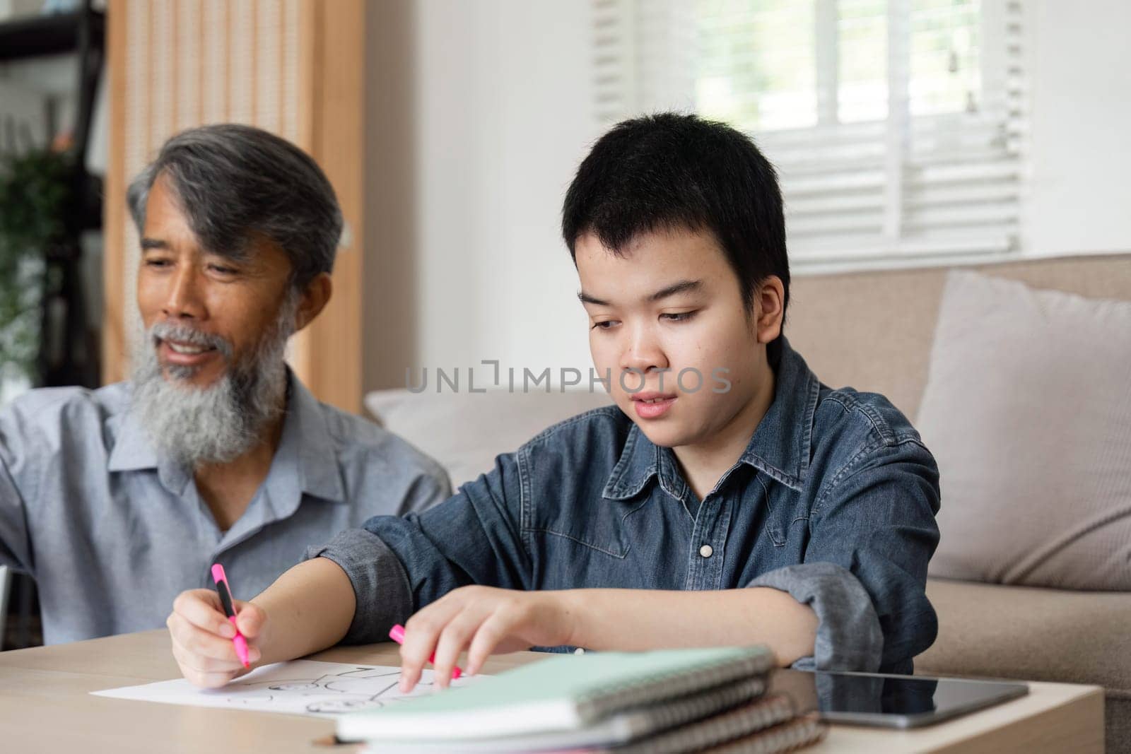 A grandfather assists his grandson with drawing, encouraging creativity and learning in a supportive home environment. Their interaction highlights the importance of family bonding.