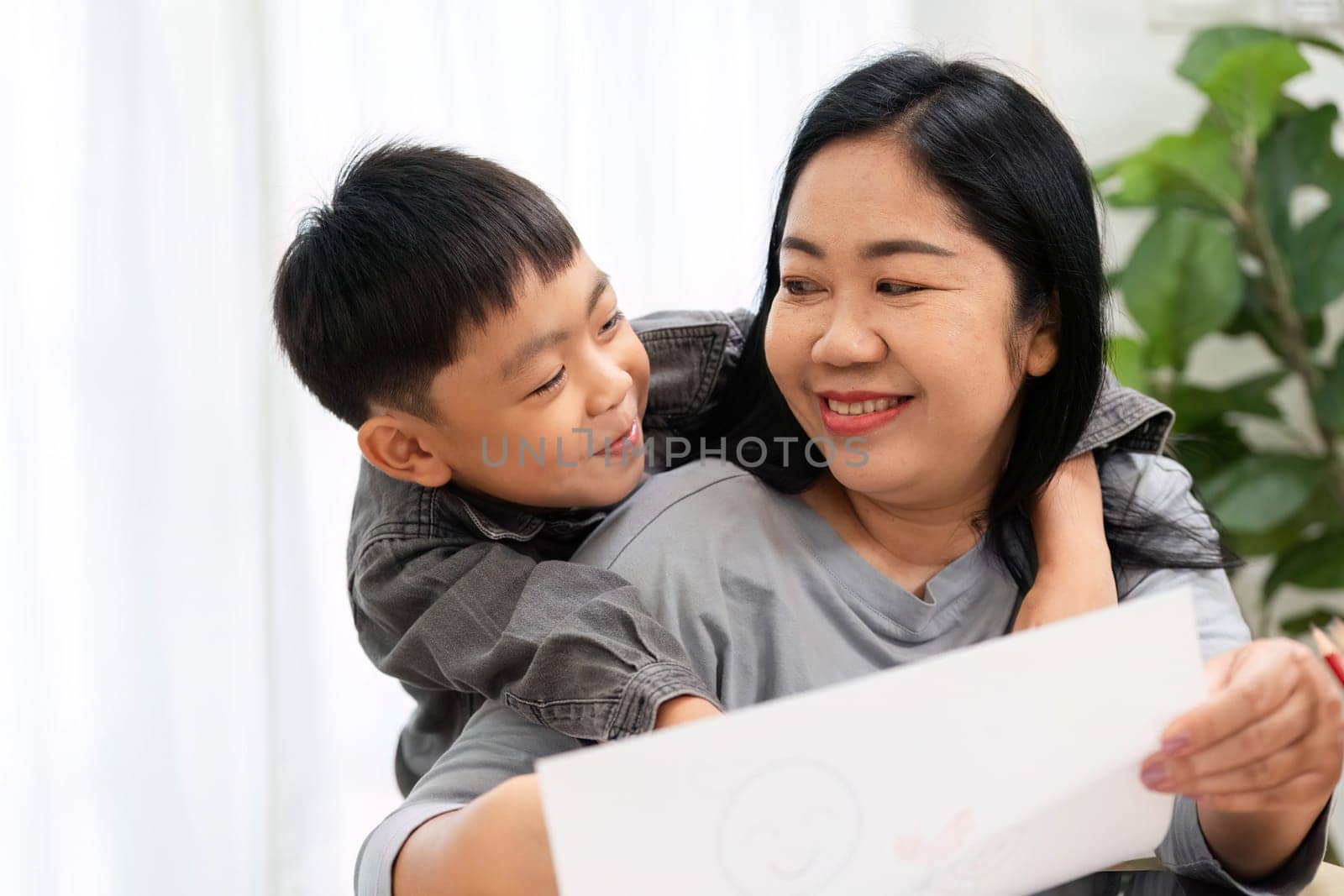 A mother and her son enjoy a creative moment together, with the boy showing off his drawing while sharing laughter and warmth in their cozy home.