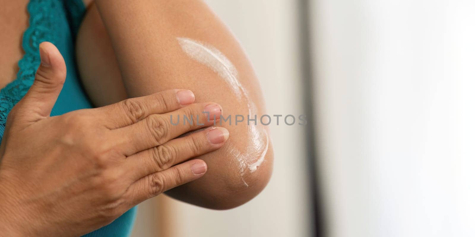 A senior woman is seen applying lotion on her elbow, emphasizing the importance of skincare and hydration in her beauty and wellness routine.