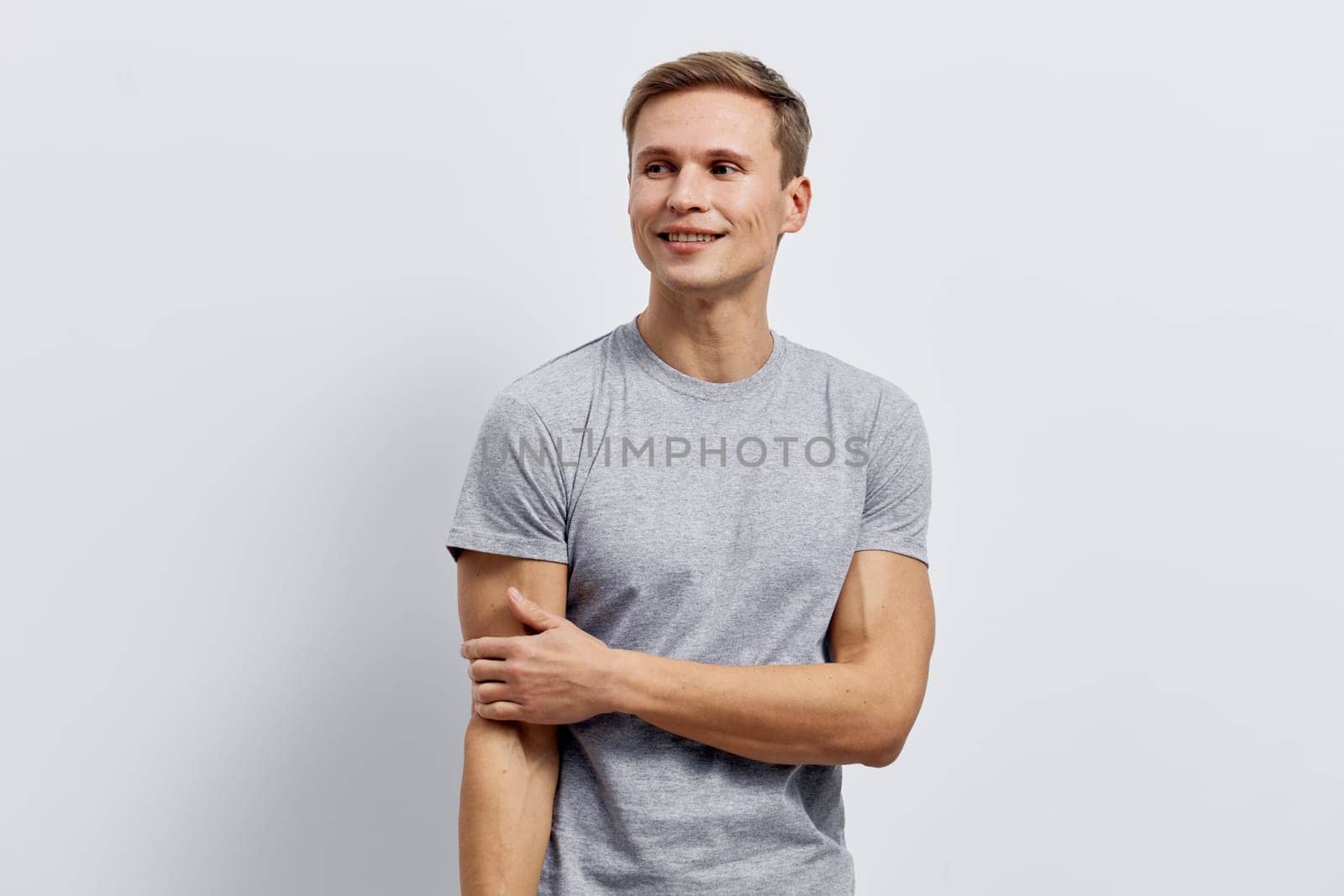 smiling man in gray t-shirt standing isolated on light background looking aside with relaxed posture and positive expression, casual style, representing digital nomad lifestyle and remote work concept focused on technology and freedom.