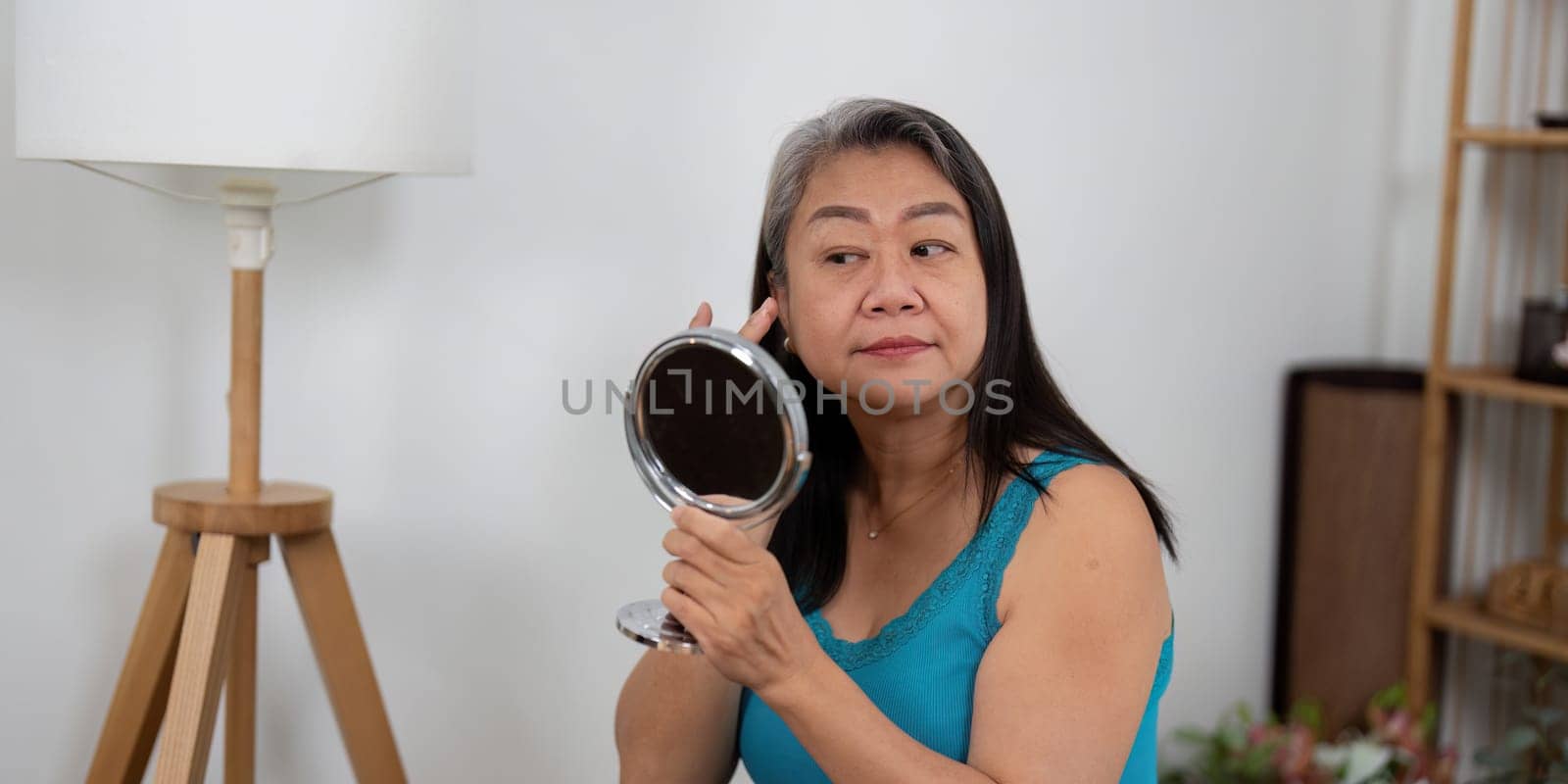 An elderly woman applies skincare while looking in the mirror, emphasizing the importance of beauty and self-care at any age. This image showcases a nurturing moment of personal care.