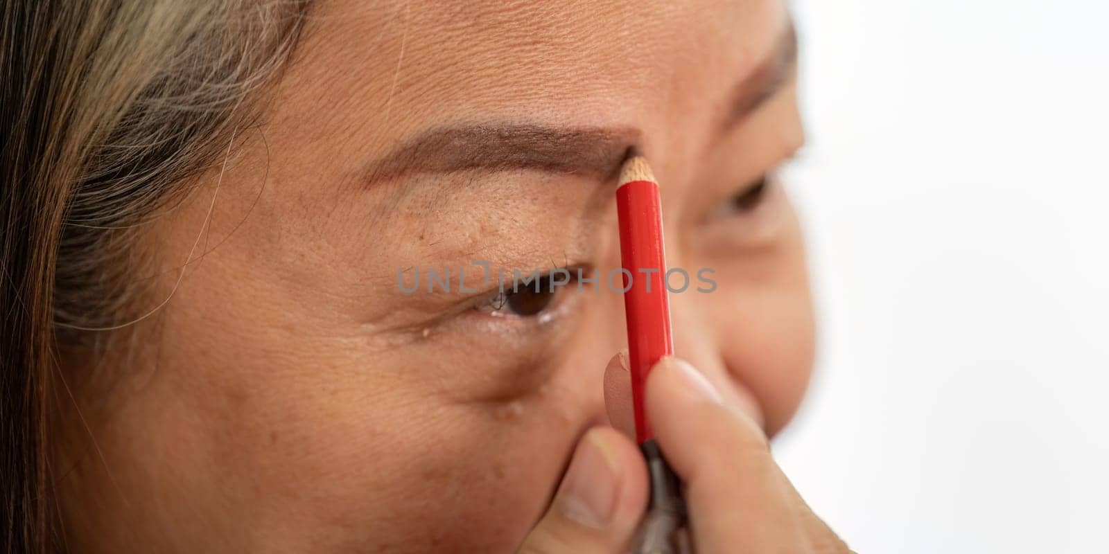 An elderly woman carefully fills in her eyebrows, showcasing her beauty routine and commitment to self-care.