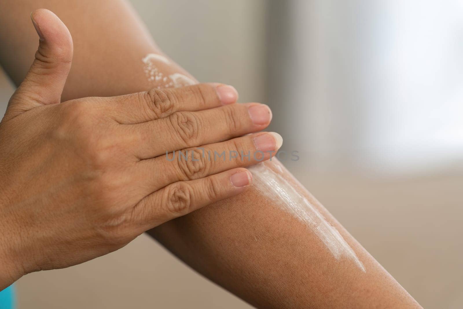 An elderly woman gently applies moisturizer to her arm, promoting skin health and hydration as part of her daily beauty and wellness routine.