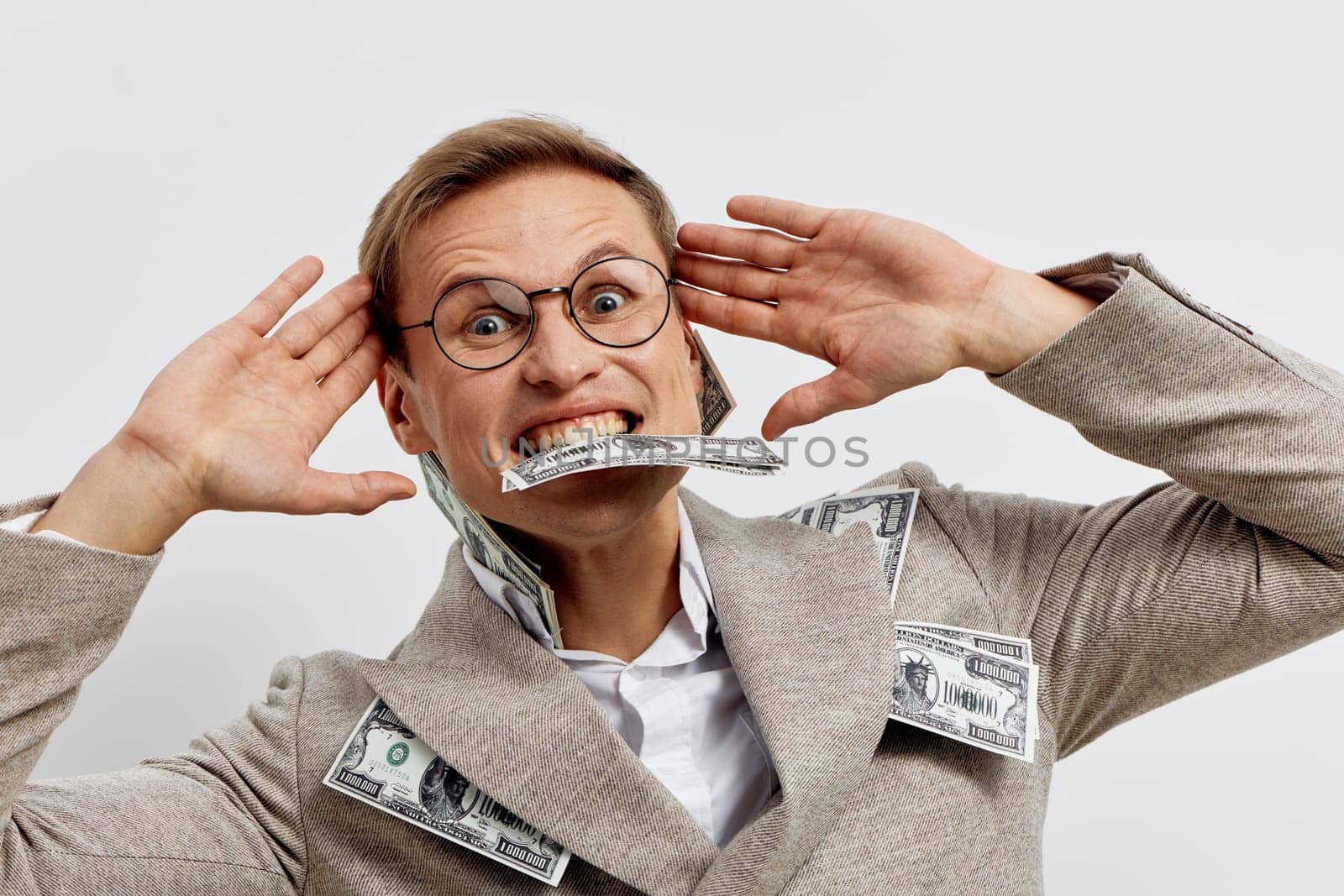 excited man with glasses in coat biting cash and holding hands near head isolated on white studio background showing success and enthusiasm related to digital nomad freelance lifestyle and remote work concept