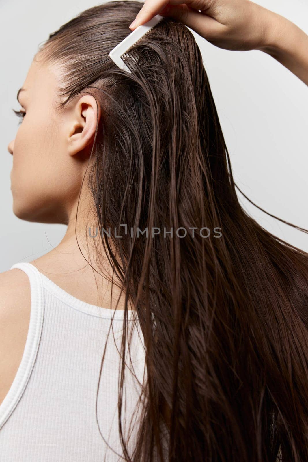 Hair care, grooming, beauty routine, personal care, long hair, combing, relaxation The image portrays a woman from the back as she styles her long, wet hair with a comb, highlighting self care and beauty