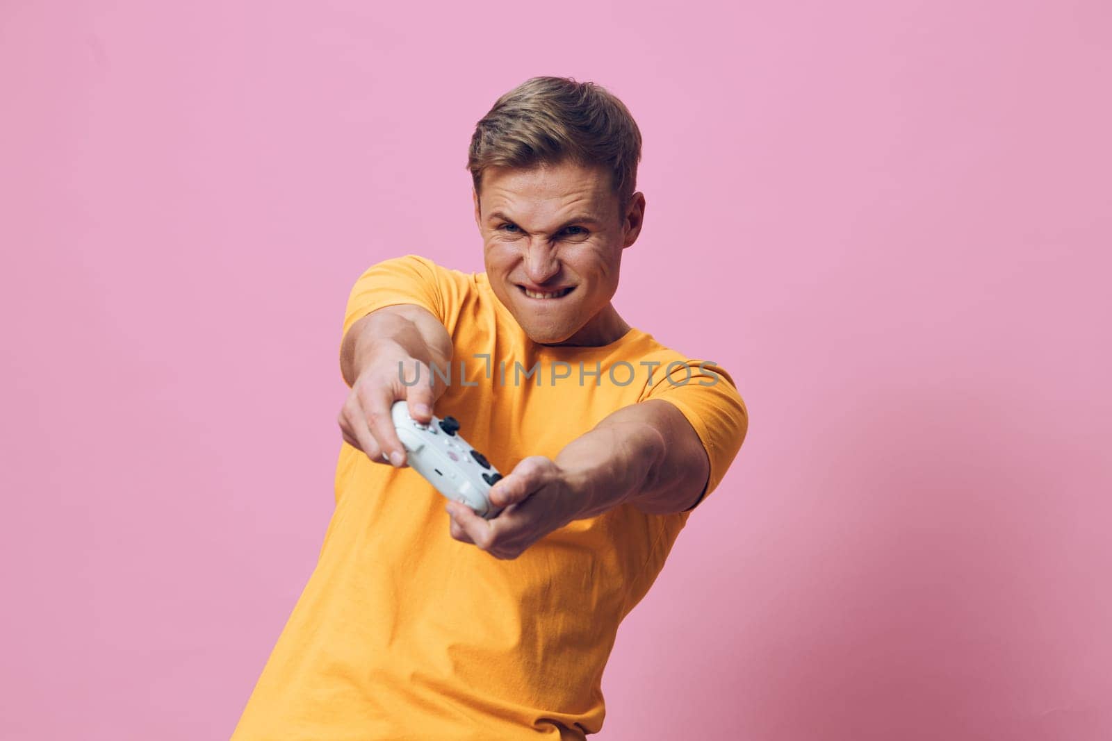 focused man playing video game with wireless controller in hands wearing yellow t-shirt isolated on pink background casual outfit intense expression esports digital entertainment concept