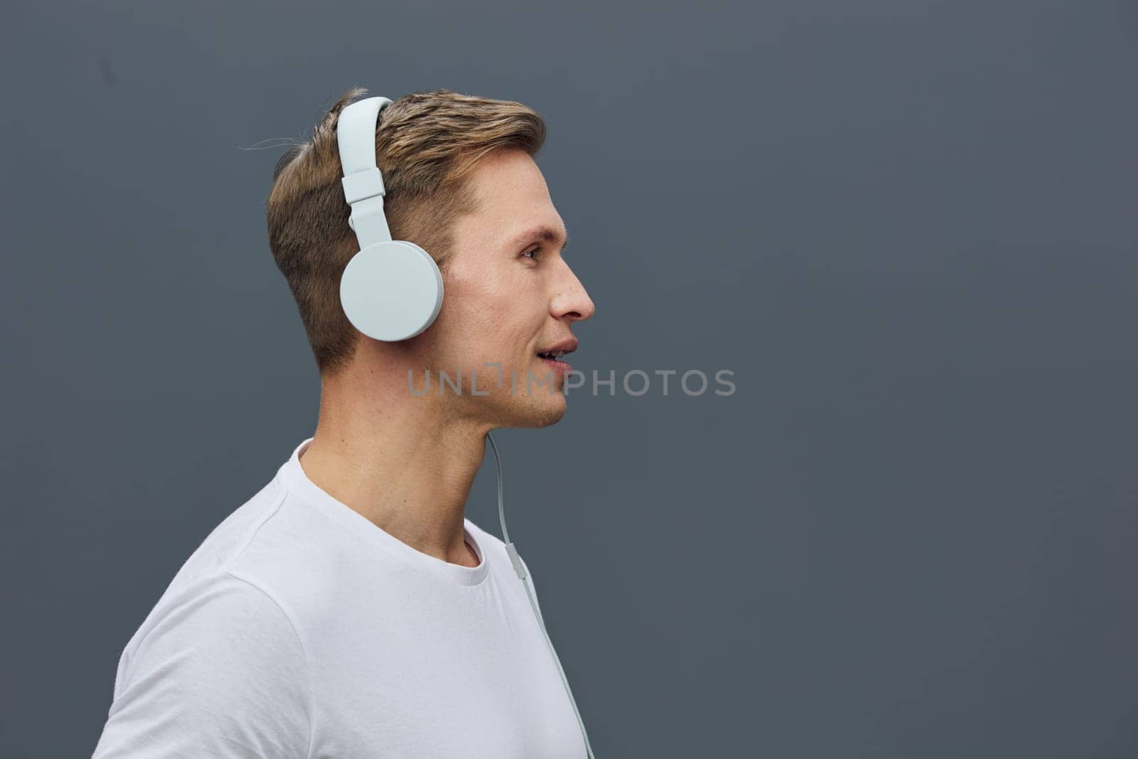 young caucasian man wearing white wireless headphones listen attentively in side profile isolated on plain grey background studio portrait focused calm digital detox mental health technology concept