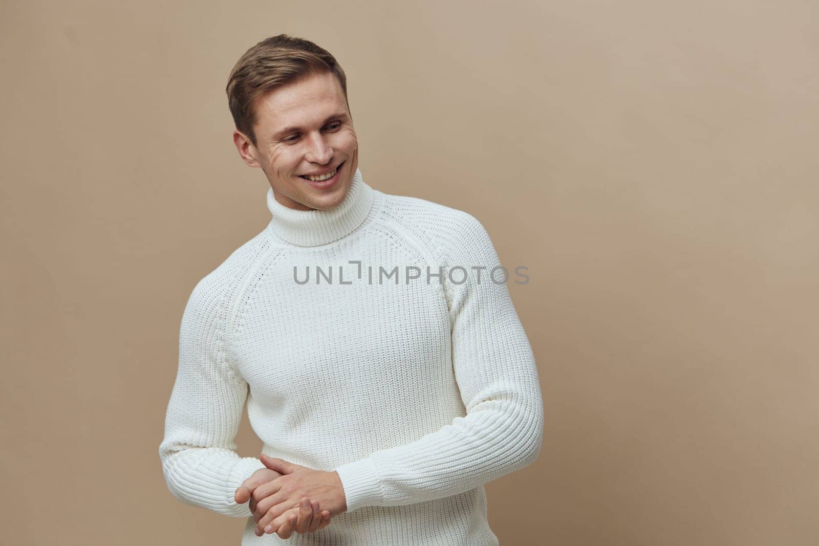 smiling caucasian man wearing white knitted turtleneck sweater looking to side with relaxed happy face against plain beige background. autumn cozy style and digital detox concept with casual warmth and comfort.