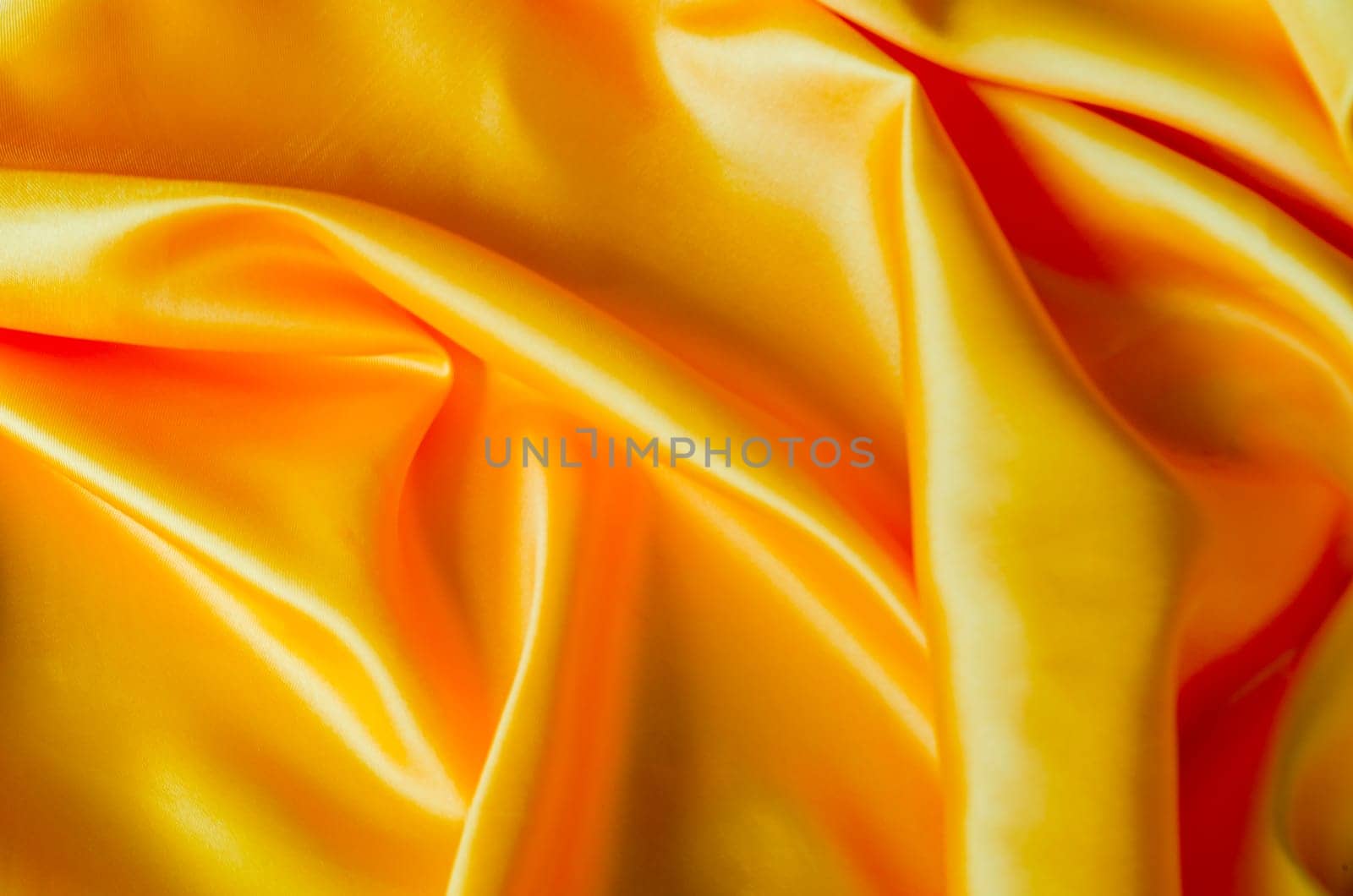 Top view of vibrant yellow color silk in soft, smooth waves with a glossy finish. Suitable for design and wallpaper background.