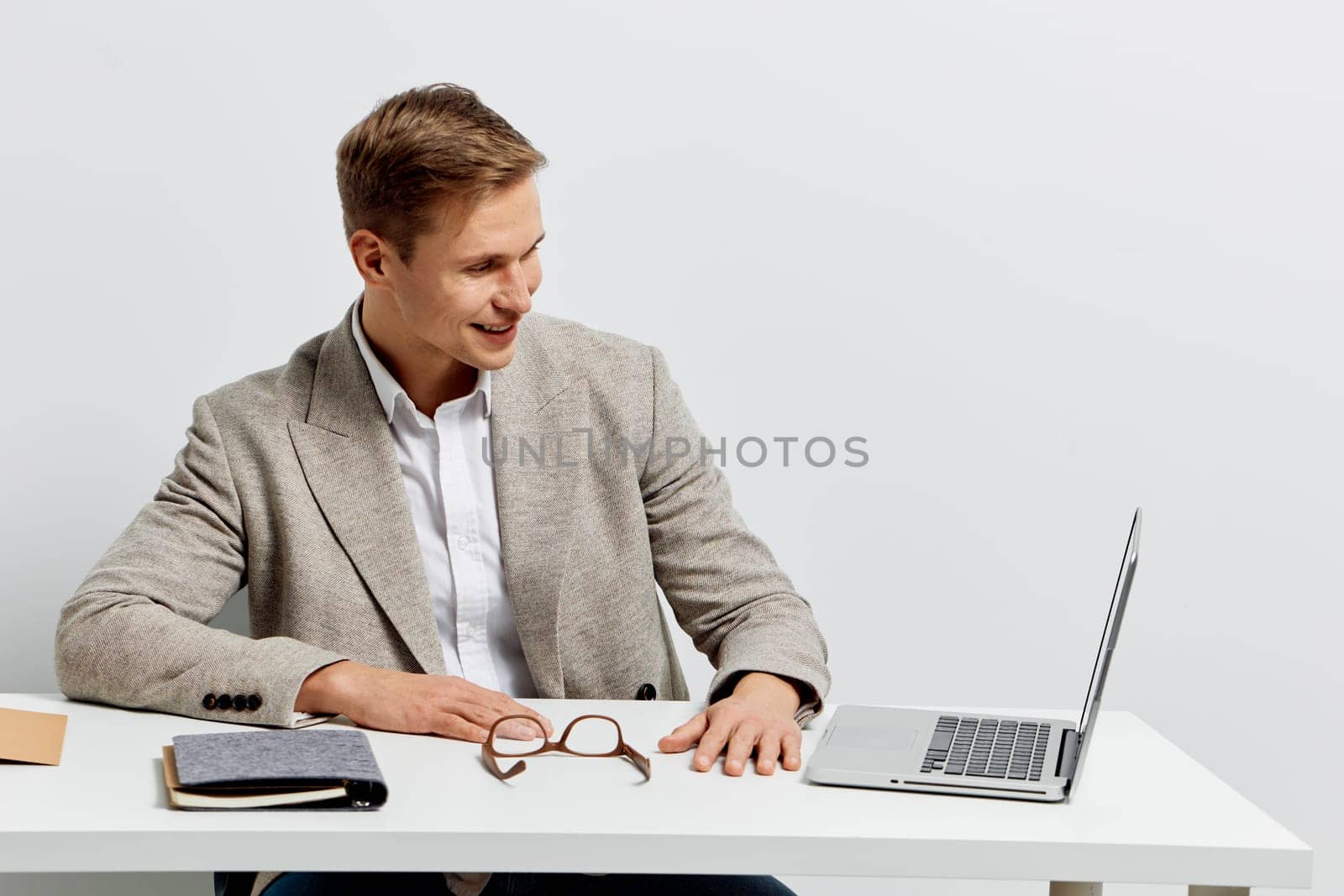 smiling man working with laptop in casual jacket sitting at desk with glasses and notebook, digital nomad lifestyle concept with technology and freedom ideas, isolated on white background