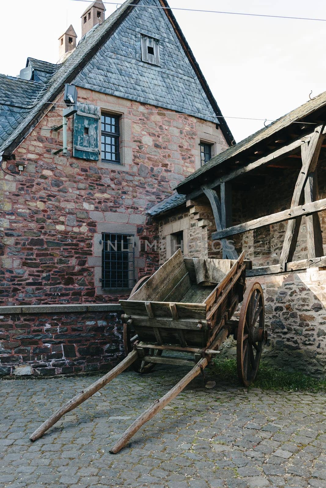 Beautiful view of old wooden medieval cart standing on stone square in old castle near stone building on spring day, side view close up. Concept of historical landmarks, time of travel and tourism.